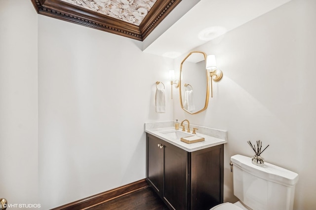 half bath with wood finished floors, vanity, baseboards, toilet, and ornamental molding