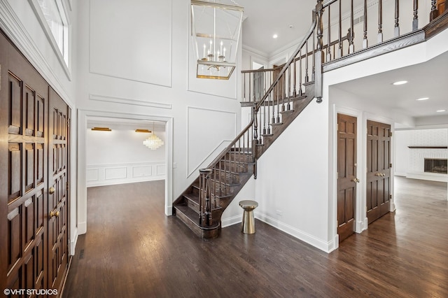 staircase with a high ceiling, a notable chandelier, wood finished floors, and a decorative wall
