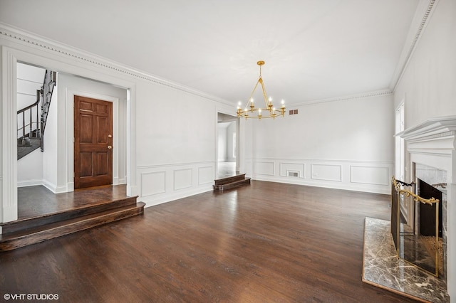 unfurnished living room featuring ornamental molding, a fireplace, wood finished floors, and a notable chandelier