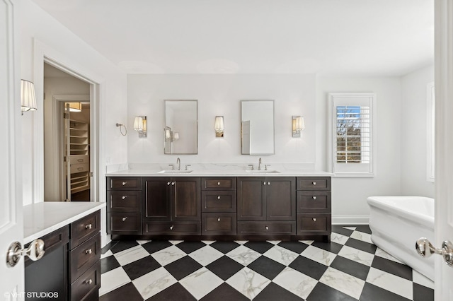 bathroom with double vanity, a sink, a walk in closet, and a soaking tub