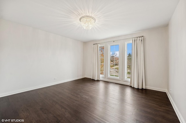unfurnished room with dark wood-style flooring, baseboards, and an inviting chandelier