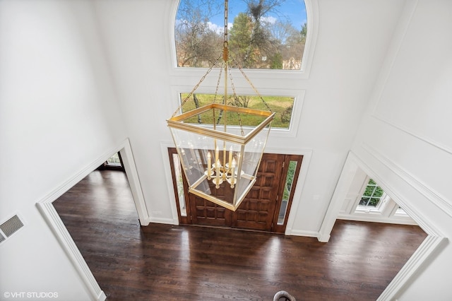 entryway featuring visible vents, a towering ceiling, wood finished floors, and a notable chandelier