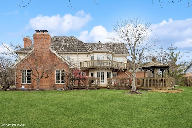 back of property with a wooden deck, a chimney, brick siding, a gazebo, and a yard