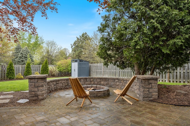 view of patio / terrace featuring an outdoor structure, a fenced backyard, a fire pit, and a shed