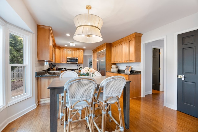 kitchen with a sink, light wood-style floors, stainless steel appliances, baseboards, and backsplash