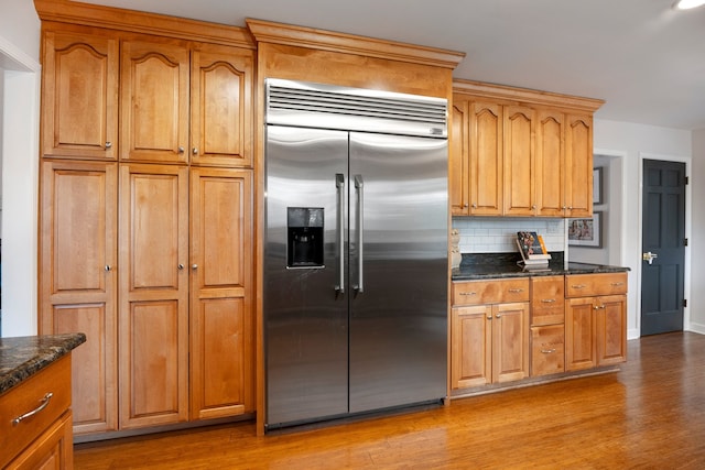 kitchen with light wood-type flooring, brown cabinetry, backsplash, and stainless steel built in refrigerator