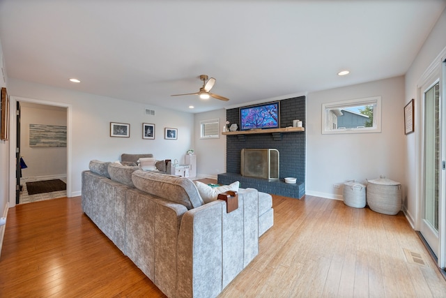 living room with a ceiling fan, a brick fireplace, hardwood / wood-style flooring, and visible vents