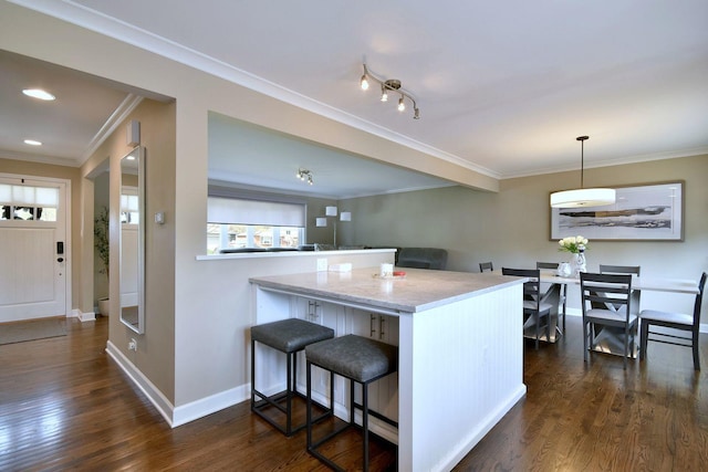 kitchen featuring baseboards, ornamental molding, a breakfast bar area, and dark wood-style floors