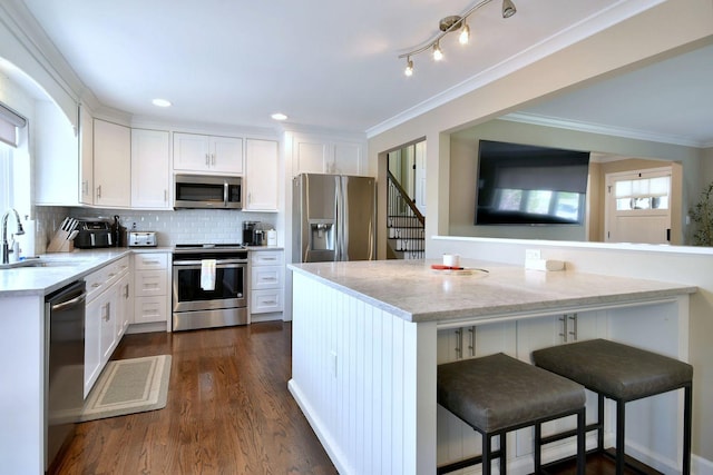 kitchen with crown molding, a sink, white cabinets, a breakfast bar, and stainless steel appliances