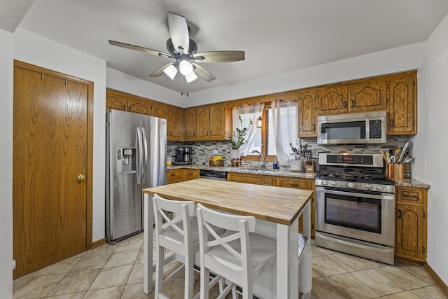 kitchen featuring brown cabinetry, light tile patterned flooring, a sink, appliances with stainless steel finishes, and backsplash