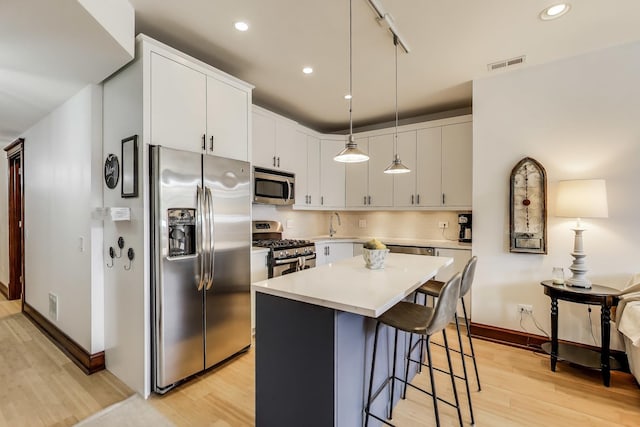 kitchen with appliances with stainless steel finishes, light wood finished floors, a breakfast bar area, light countertops, and visible vents