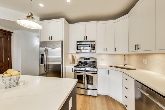 kitchen with a sink, appliances with stainless steel finishes, hanging light fixtures, and backsplash