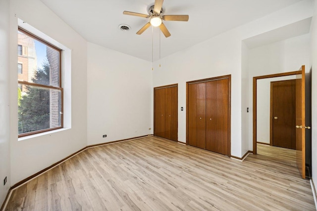 unfurnished bedroom with visible vents, multiple closets, baseboards, light wood-type flooring, and a ceiling fan