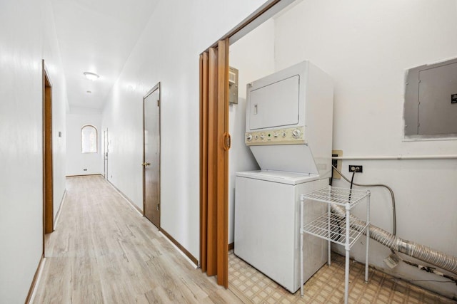 laundry room with electric panel, laundry area, stacked washer and dryer, baseboards, and light floors