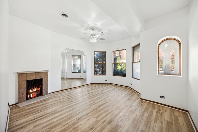 unfurnished living room with ceiling fan, baseboards, wood finished floors, a tile fireplace, and visible vents