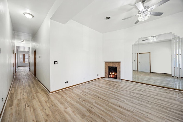unfurnished living room featuring a tiled fireplace, light wood-style flooring, a ceiling fan, baseboards, and visible vents