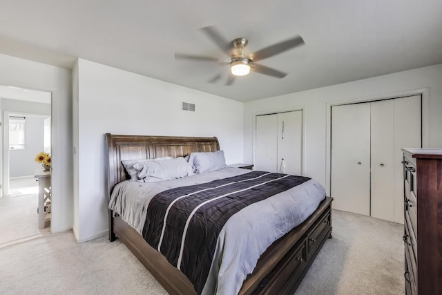 bedroom featuring visible vents, a ceiling fan, multiple closets, and light carpet