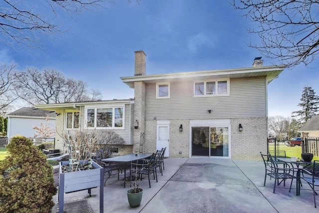rear view of property with fence, brick siding, outdoor dining area, a chimney, and a patio area
