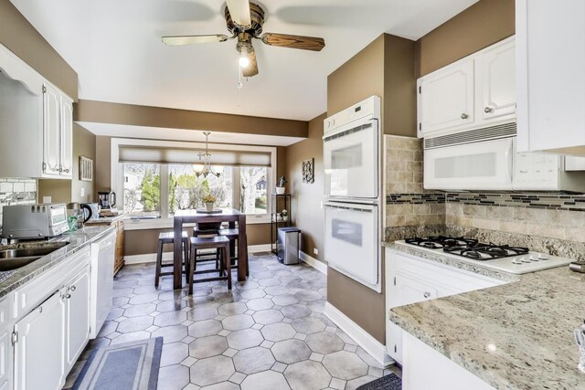 kitchen with white appliances, baseboards, ceiling fan, white cabinetry, and backsplash