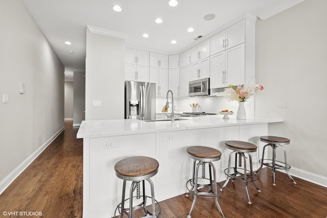 kitchen with a sink, stainless steel appliances, baseboards, recessed lighting, and a peninsula