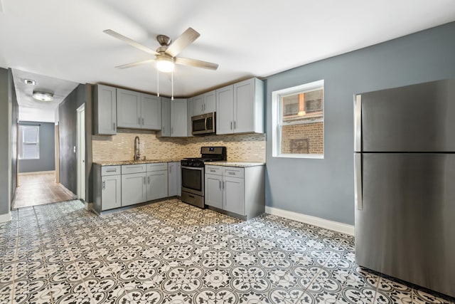 kitchen with appliances with stainless steel finishes, a sink, gray cabinets, baseboards, and backsplash