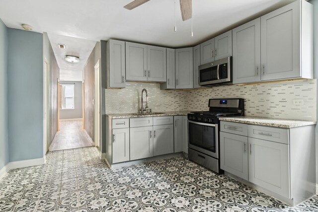 kitchen featuring appliances with stainless steel finishes, a sink, gray cabinets, baseboards, and decorative backsplash