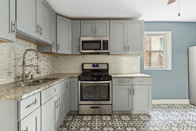 kitchen featuring decorative backsplash, light stone counters, a sink, gray cabinetry, and stainless steel appliances