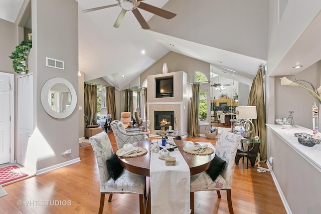 dining room featuring a ceiling fan, a tiled fireplace, wood finished floors, high vaulted ceiling, and recessed lighting