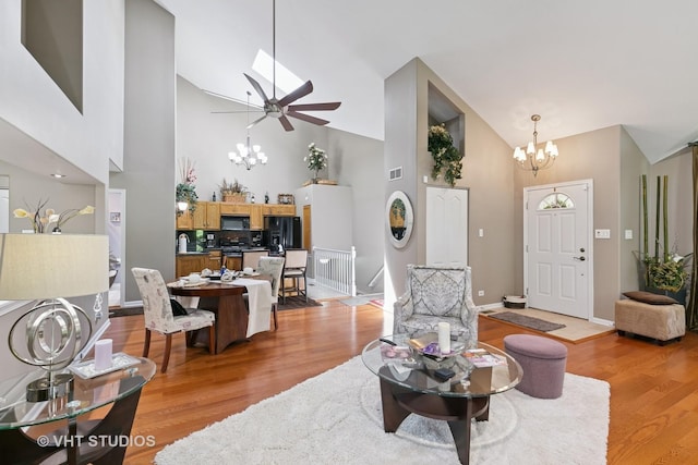 living area featuring a chandelier, high vaulted ceiling, light wood finished floors, baseboards, and a ceiling fan