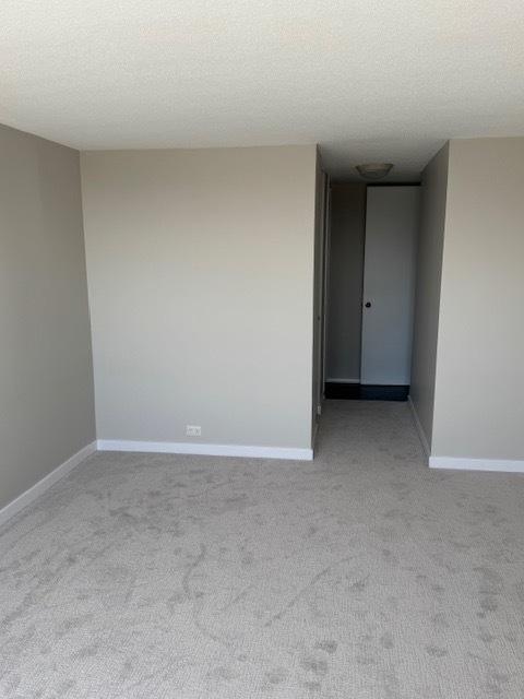 empty room with baseboards, a textured ceiling, and light colored carpet