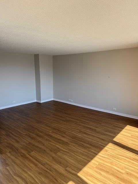 spare room featuring a textured ceiling, baseboards, and dark wood-type flooring