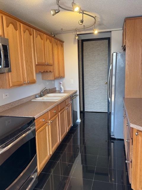 kitchen with a sink, appliances with stainless steel finishes, dark tile patterned flooring, and light countertops