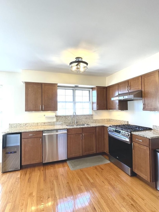 kitchen with light stone countertops, light wood-type flooring, a sink, under cabinet range hood, and stainless steel appliances