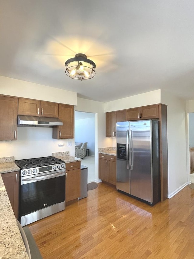 kitchen featuring light wood-type flooring, baseboards, light stone counters, under cabinet range hood, and stainless steel appliances