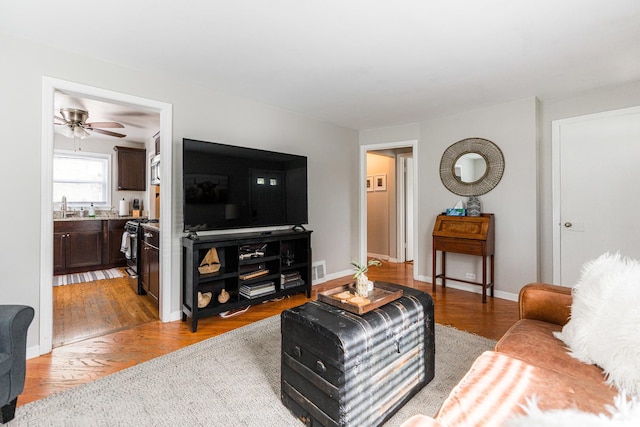 living area featuring light wood-style floors, baseboards, and ceiling fan