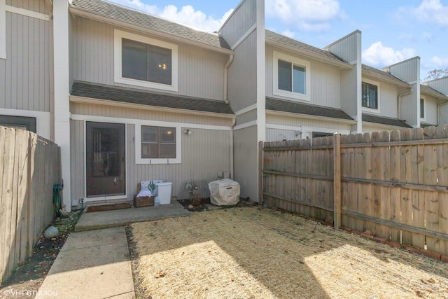 back of property with a fenced backyard and a shingled roof
