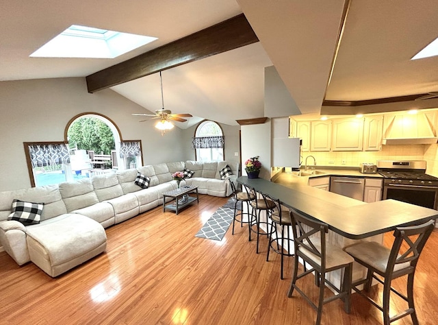 living room with light wood-style floors, plenty of natural light, a ceiling fan, and lofted ceiling with skylight