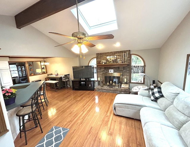living area with a brick fireplace, a skylight, beam ceiling, and wood finished floors