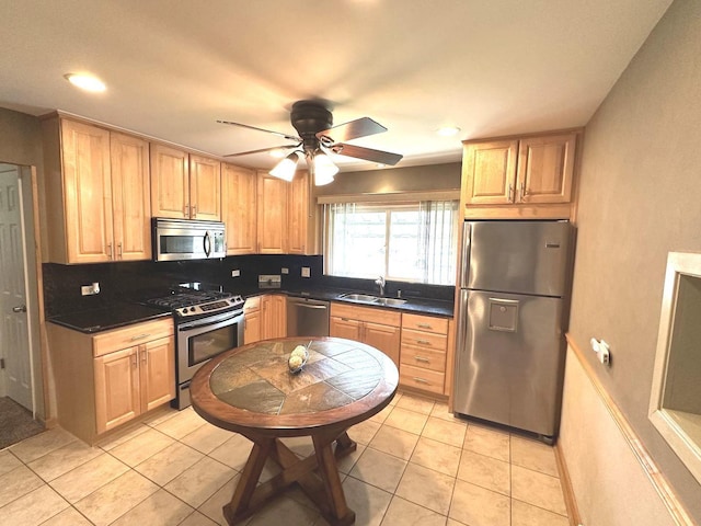 kitchen featuring dark countertops, appliances with stainless steel finishes, a sink, light brown cabinets, and a ceiling fan