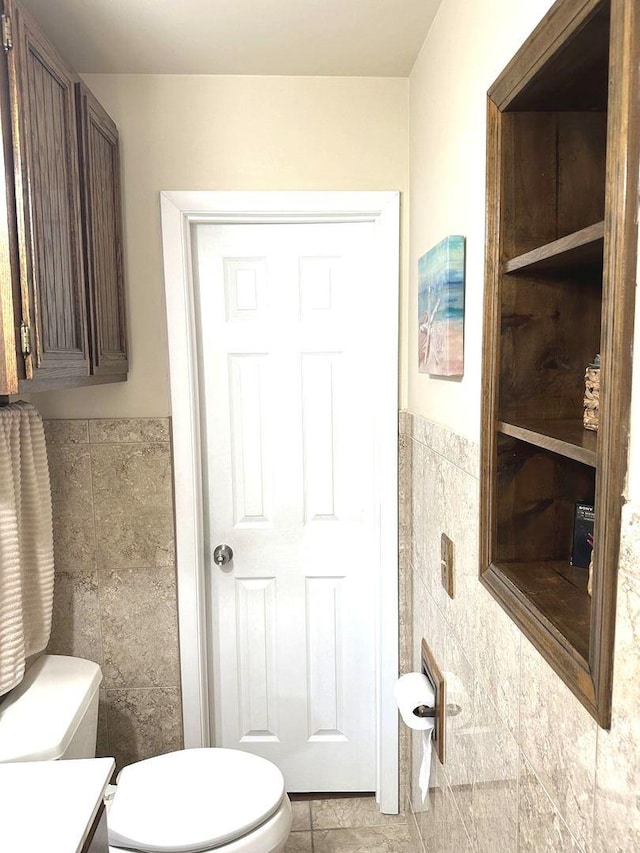 bathroom with toilet, tile patterned floors, tile walls, and wainscoting