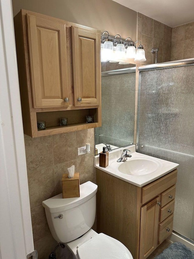 full bathroom featuring toilet, a shower with door, tile walls, and vanity