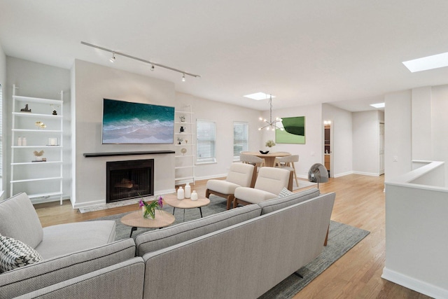 living room with an inviting chandelier, track lighting, light wood-style flooring, a fireplace with flush hearth, and a skylight