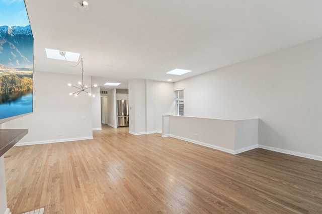 unfurnished living room with baseboards, a skylight, an inviting chandelier, and wood finished floors