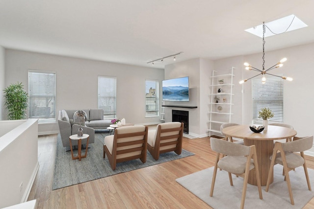 living room featuring a skylight, a fireplace, baseboards, light wood finished floors, and a notable chandelier
