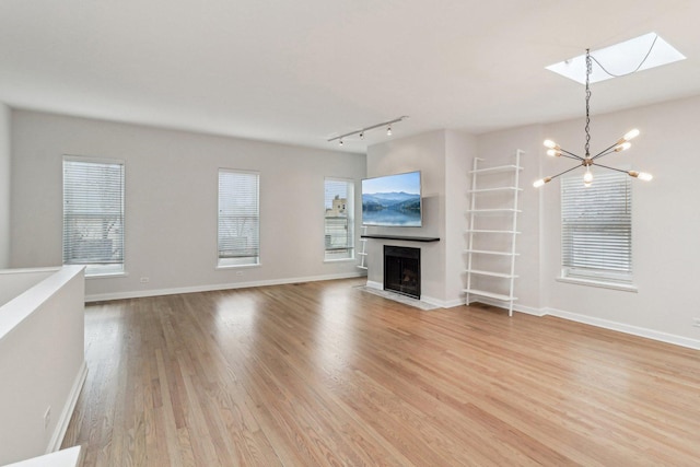 unfurnished living room with an inviting chandelier, light wood finished floors, baseboards, a fireplace with flush hearth, and a skylight
