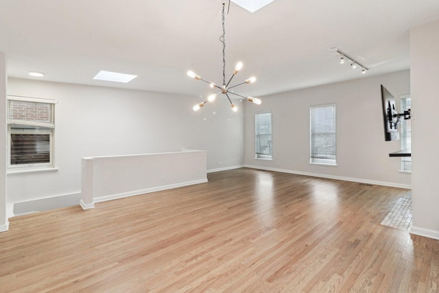 unfurnished dining area with an inviting chandelier, track lighting, baseboards, light wood finished floors, and a skylight