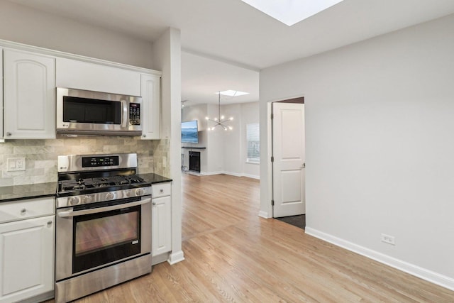 kitchen featuring dark countertops, white cabinets, backsplash, a skylight, and stainless steel appliances