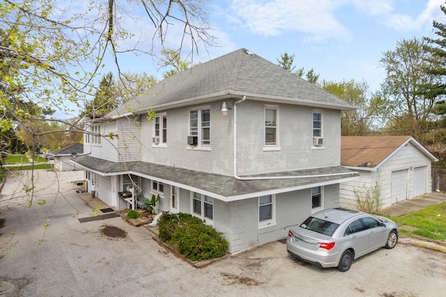 view of front of house featuring a shingled roof, brick siding, cooling unit, and a detached garage