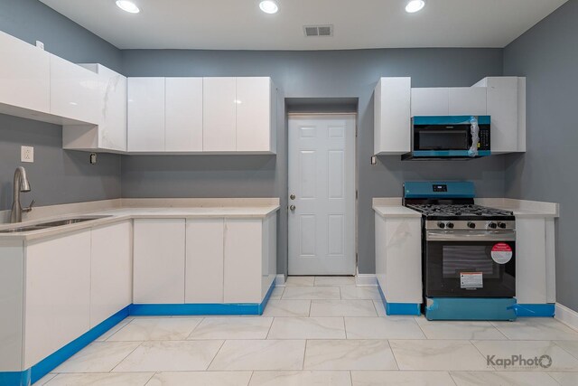 kitchen with light countertops, white cabinetry, a sink, and stainless steel gas range oven