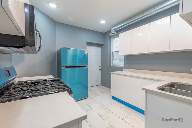 kitchen with a sink, light stone counters, stainless steel gas range, freestanding refrigerator, and white cabinetry